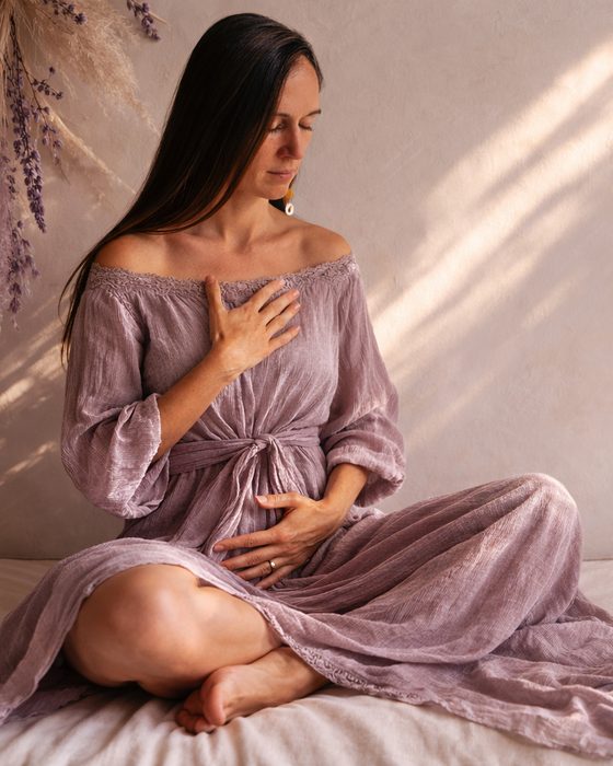 Monja im fliederfarbenen Kleid, eine Hand auf dem Herzen, eine auf dem Bauch