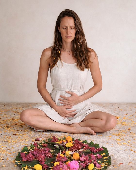 Monja sitzt im Schneidersitz vor einem Blumenmandala, die Hände auf dem Bauch